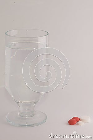 Glass of water beside red and white pills. Taking drugs concept. Stock Photo