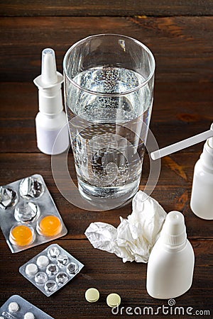 A glass of water, a spray for the nose, nasal drops, pills in the blister, candy from the cough on the table. Modern medicines for Stock Photo