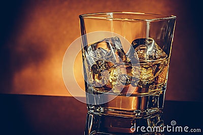 Glass of whiskey on black table with reflection and gold background, warm atmosphere Stock Photo