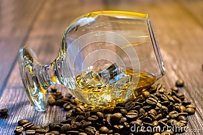 A glass of whiskey with ice and coffee beans on a wooden table. Strong alcohol with ice. Vintage close-up of golden cognac. Stock Photo