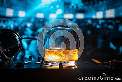 Glass with whisky with ice cube inside on dj controller at nightclub. Dj Console with club drink at music party in nightclub with Stock Photo