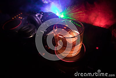 Glass with whisky with ice cube inside on dj controller at nightclub. Dj Console with club drink at music party in nightclub with Stock Photo