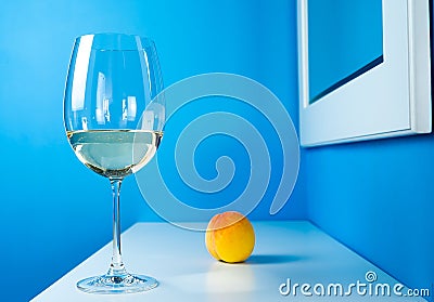 A glass of white wine on a blue background is standing on a white table with a peach Stock Photo