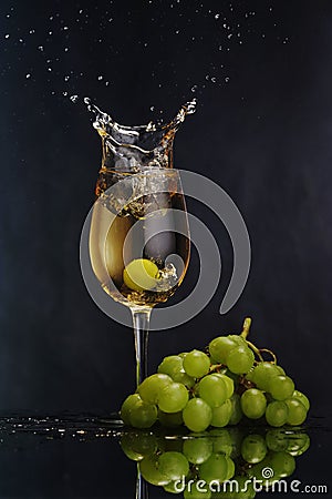 A glass of white wine on a dark background. Splash white wine. Grape bunch Stock Photo