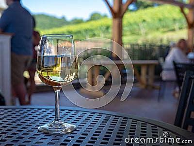 A glass of white wine sitting on patio table in a shaded outdoor dining area Stock Photo