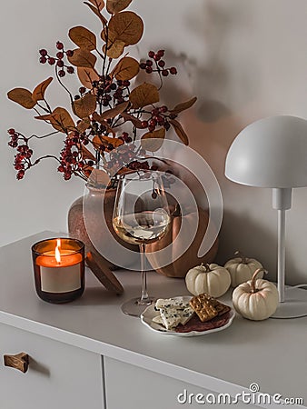 A glass of white wine, a snack, autumn decor on a white chest of drawers in a cozy living room Stock Photo