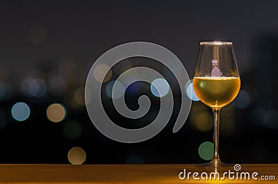 A glass of white wine on wooden table of rooftop bar with colorful bokeh of city light and space for text Stock Photo