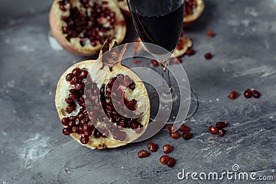 A glass of wine on a gray background among pomegranates. Close pomegranate and red pomegranate seeds Stock Photo