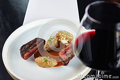 A glass of wine, a plate with pieces of meat of beef steak and broccoli Stock Photo