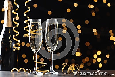 Glasses and bottle of champagne with serpentine streamers against blurred lights on black background. Space for text Stock Photo