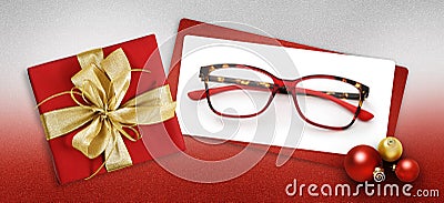Glasses christmas gift card, red box with shiny golden ribbon bow, white ticket and eyewear near xmas balls on glittering red Stock Photo