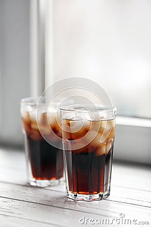 Glasses of cola with ice near window Stock Photo