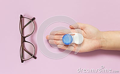 Glasses and contact lens case in human hand on purple background. Concept of choice the way vision correction Stock Photo