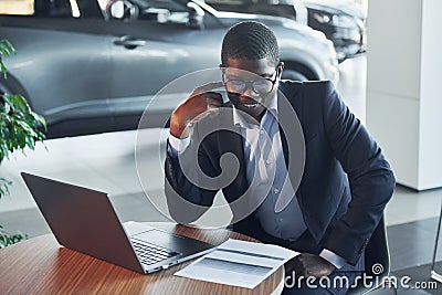 In glasses. Office worker is sitting in autosalon by table with laptop Stock Photo