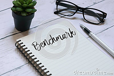 Glasses,plant,pen and notebook written with Benchmark on white wooden background. Stock Photo