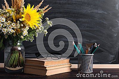 Glasses teacher books and wildflowers bouquet on the table, on background blackboard with chalk. The concept of the teacher`s day Stock Photo