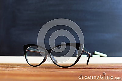 Glasses teacher on a table, against a chalkboard background with chalk. Concept for teachers day. Copy space. Stock Photo