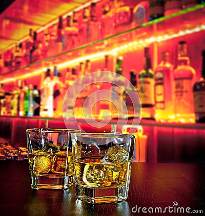 Glasses of whiskey with ice on bar table near whiskey bottle on warm atmosphere Stock Photo