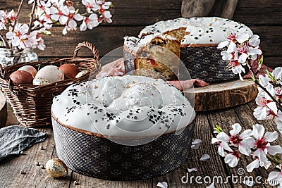 Glazed Easter cake or bread kulich decorated with candy on rustic wooden table with colored easter eggs in basket and spring Stock Photo