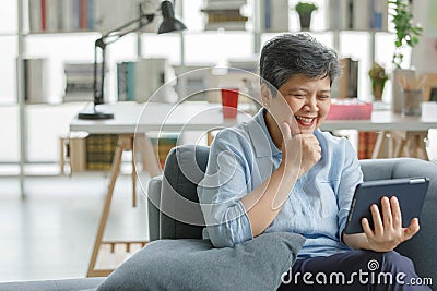 Gleeful Asian female using tablet at home Stock Photo