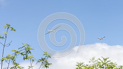 Glider pulled by a small plane, seen above the trees, in a blue sky with fluffy clouds Stock Photo