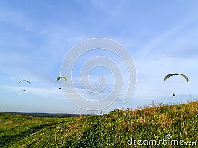 Gliding parachutes flying in blue sky above green hill with grass and path Stock Photo