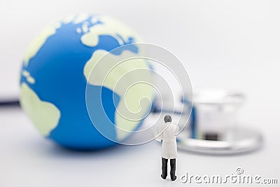 Global Health Care Concept. Close up of doctor miniature figure stanind with patient chart with mini world ball and Stethoscope Stock Photo