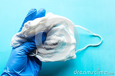 Gloved hand holds medical mask over blue background. Stock Photo