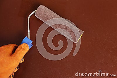 Gloved hand holds a paint roller on a dark brown background Stock Photo