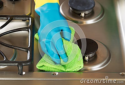 Gloved hand wiping down stove top range with green microfiber ra Stock Photo