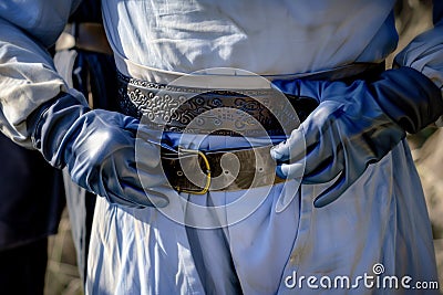 gloved hands fastening a sword belt around waist Stock Photo