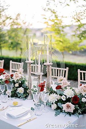 Glowing candles in candlesticks with glass caps stand on a festive table among flowers Stock Photo