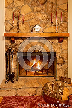 A warm fire in a beautiful stone fireplace with clock and candelabras on the mantle. Stock Photo