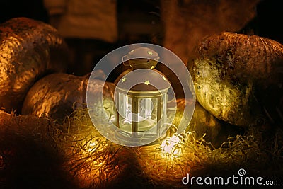 Glowing lantern on hay bale and golden pumpkins in dark, mystical atmospheric image. Modern festive halloween street decor, candle Stock Photo