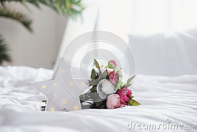 Glowing LED star and a bouquet of artificial peonies on a white bed in the interior Stock Photo