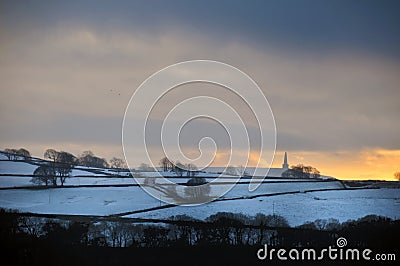 Glowing orange sunset in a cloudy twilight winter sky with snow covered fields with stoodley pike monument in the distance in Stock Photo