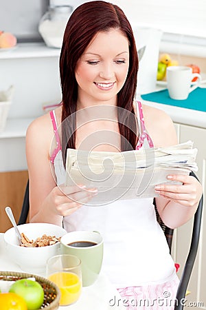 Glowing woman eating cereals and reading newspaper Stock Photo