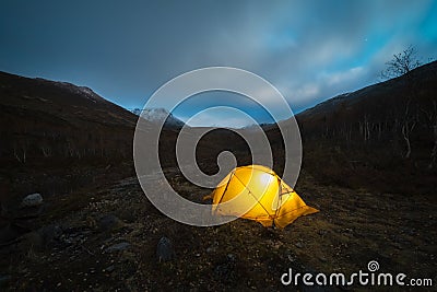 Glowing Yellow Tent and Clouds in Khibiny Mountains at Autumn Night. Russia Stock Photo