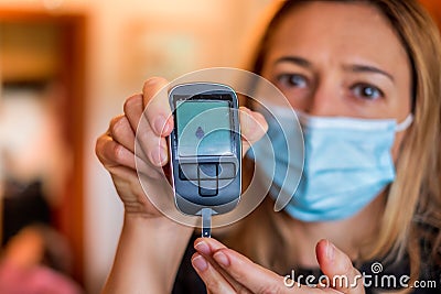 Glucometer device for glucose test with dripped blood in diabetic patients held by the blonde nurse with surgical mask Stock Photo