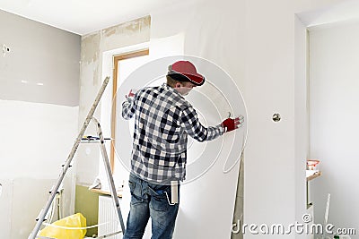 Glueing wallpapers at home. Young man, worker is putting up wallpapers on the wall. Home renovation concept Stock Photo