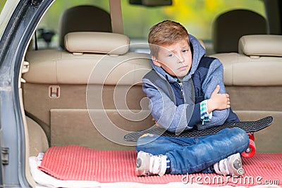 Glum little boy sitting in the boot of a car. Stock Photo