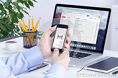 Gmail app on iPhone display in man hands and on Macbook screen Editorial Stock Photo