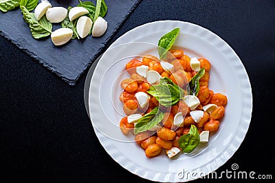 Gnocchi alla Sorrentina in tomato sauce with green fresh basil and mozzarella balls served on a plate Stock Photo