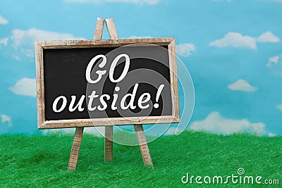 Go Outside message on standing chalkboard on grass with sky Stock Photo