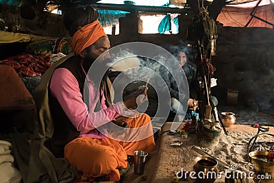 hermit sadhu smokes a narcotic compound sitting in a hut emitting a large tangle of smoke. Babba ascetic lives in poor conditions Editorial Stock Photo