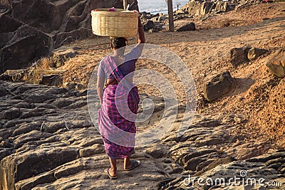 GOA, INDIA - MARCH 4: Woman in saris with basket on her head walks by Vagator beach on March 4, 2017 in Goa, India Editorial Stock Photo