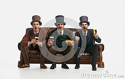 Portrait with three friends wearing old-fashioned clothes sitting on sofa with snack and tense face over white Stock Photo