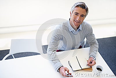 Goals are dreams with a plan and a deadline. Portrait of a businessman sitting with his cellphone and notebook at his Stock Photo
