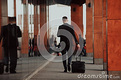 Going to airport terminal. Confident businessman traveler walking on city streets and pulling his suitcase drinking Stock Photo