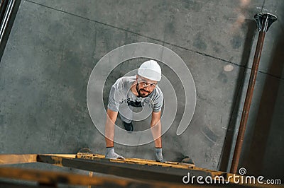 Going up on the ladder, top view. Young factory worker in grey uniform Stock Photo